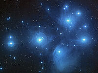 Auf dem Bild ist eine lockere Ansammlung von Sternen zu sehen. Die Sterne sehen bläulichen aus. Das sind die „Plejaden“. In der Astronomie sagt man zu so etwas „Offener Sternhaufen“. Wenn man das Bild anklickt, wird es größer dargestellt.