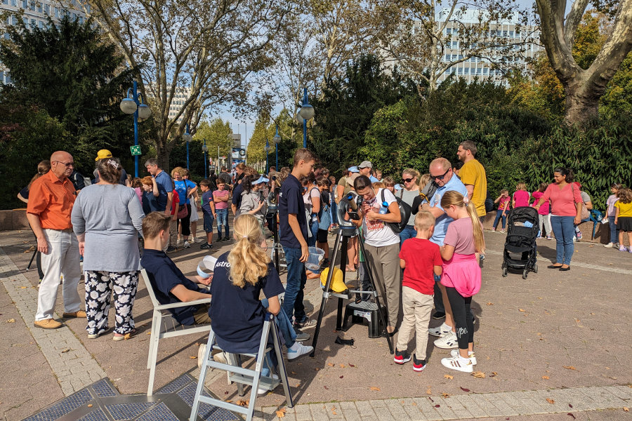 Das Bild zeigt Menschen auf dem Vorplatz des Planetariums beim Beobachten der Sonne unter Anleitung der AstroScouts des Planetarium Mannheim.