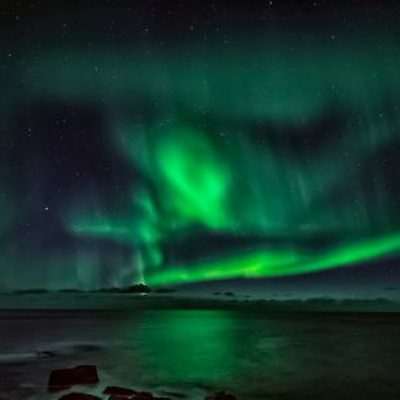 Link zur Beschreibung der aktuellen Ereignisse am Sternhimmel – Das Bild zeigt eine Winterlandschaft, über der grünes Polarlicht am Nachthimmel leuchtet. Das Polarlicht spiegelt sich auf der Oberfläche eines Sees im Bildvordergrund.