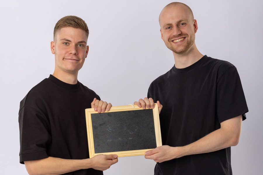 Auf dem Bild sind die Vortragenden Johannes Mensing und Josef Naber zu sehen. Sie halten zusammen eine kleine Schultafel zwischen sich.