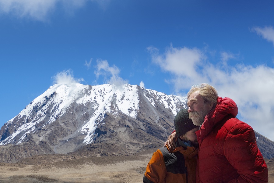 Das Bild zeigt Achill und Aaron Moser vor der Besteigung des Kilimandscharo. Im Hintergrund ist der Kilimandscharo mit schneebedecktem Gipfel zu sehen..
