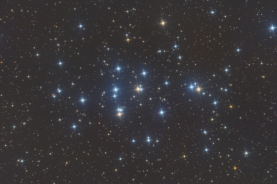 Das Bild zeigt den offenen Sternhaufen M44 („Praesepe“) im Sternbild Krebs. Im Hintergrund sind viele schwach leuchtende Sterne. Im Vordergrund stehen etliche helle Sterne nah beieinander. Sie sind Teil des Sternhaufens und leuchten bläulich und rötlich.  