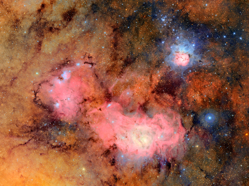 Link zur Beschreibung des Vortrags „Neues von den Sternen“ am 02.10.2025 - Das Bild zeigt leuchtende Nebel im Sternbild Schütze: den langgestreckten rötlichen Lagunennebel und den kleinen rötlich-bläulichen Trifidnebel. 