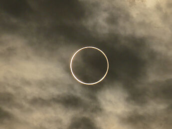 Das Bild zeigt eine ringförmige Sonnenfinsternis. Der Mond bedeckt die Sonne dabei nicht vollständig, so dass um einen dunklen kreisförmigen Bereich, der den größten Teil der Sonnenscheibe verdeckt, ein schmaler heller Ring leuchtet.