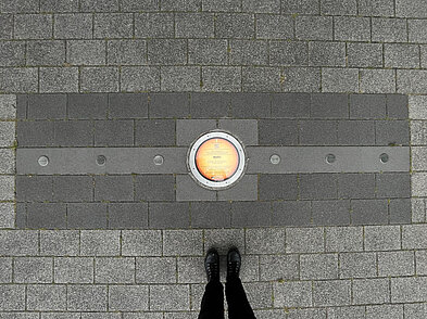 Planetenscheibe, die die Position der Erde in der Planetenallee in der Augustaanlage in Mannheim symbolisiert, von oben. Der Abstand zwischen Nägeln links und rechts der Scheibe markiert die Strecke, die die Erde an einem Tag auf ihrer Bahn zurücklegt.